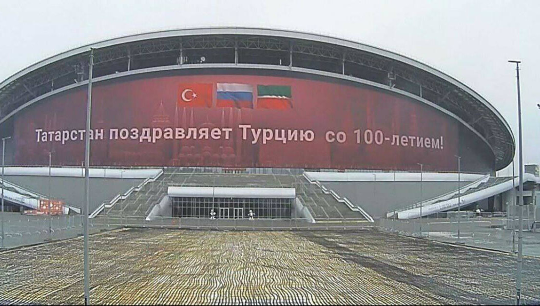 На красном фоне изображены три флага: России